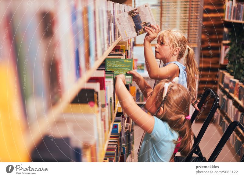 Schoolgirls looking for books in school library. Students choosing set books. Elementary education. Doing homework. Back to school back schoolgirl child reading