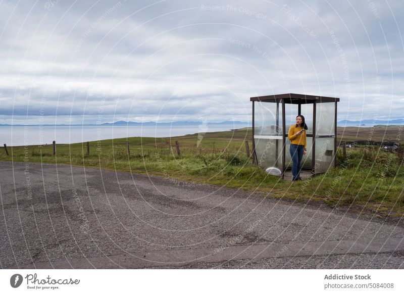 Woman standing in bus stop near road on Skye Island woman traveler countryside hillside greenery overcast nature skye island cloud trip casual female journey