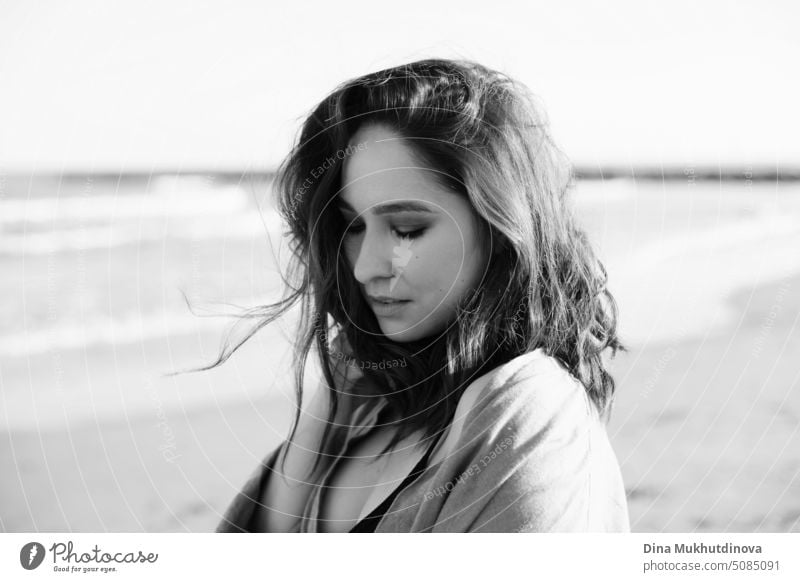 Portrait of beautiful caucasian woman with brown hair at the beach by the sea looking away. Black and white monochrome romantic portrait of attractive woman. Book cover.