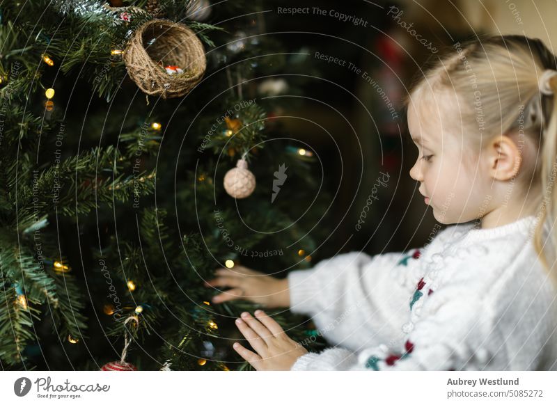 Toddler girl with pigtails putting ornaments on a christmas tree Santa Claus background blonde bright celebration child childhood cute december decoration