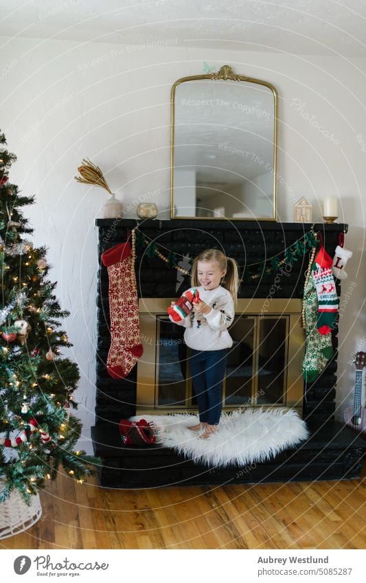 toddler girl with blonde pigtails and a winter sweater finding socks in her Christmas stocking Santa Claus background black fireplace bright celebration child