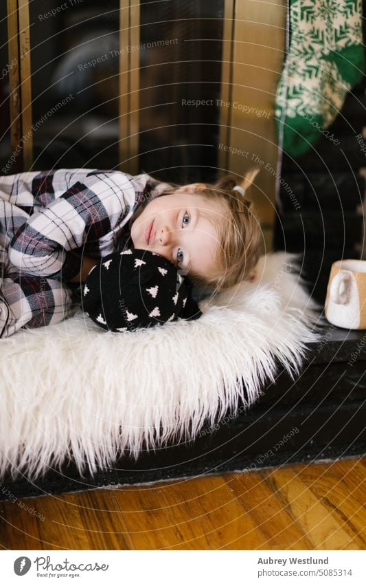 Little blonde girl wearing plaid pajamas cuddling with her stuffed animal on a black fireplace Santa Claus background bright celebration child childhood