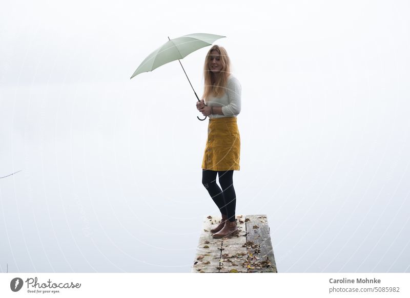 Young woman standing with green umbrella on jetty by lake on foggy morning Fog Misty atmosphere Umbrellas & Shades Shroud of fog Landscape Nature Exterior shot