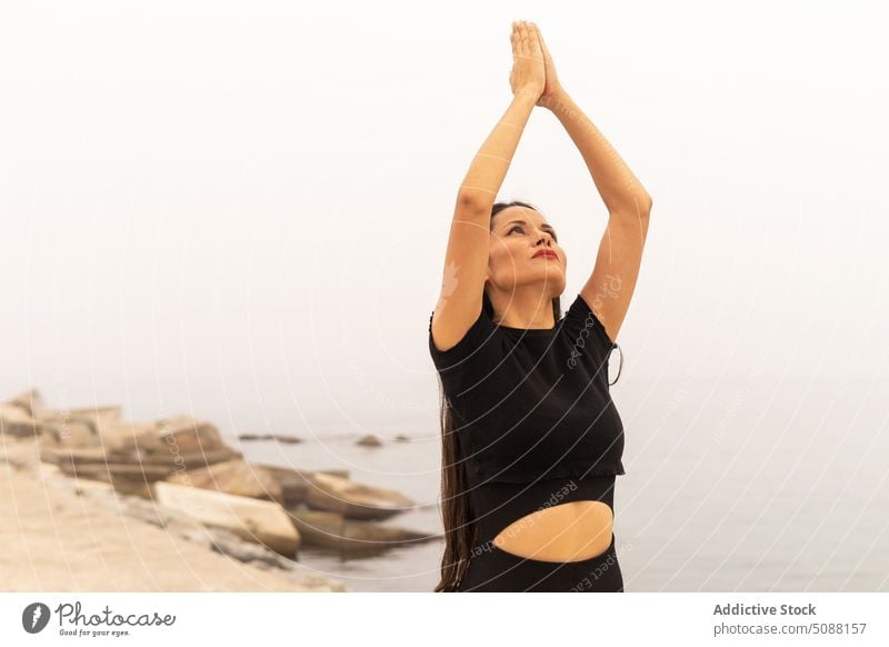 Slim woman doing yoga raising hands in namaste gesture practice asana crescent lunge ashta chandrasana sea fog harmony calm fit female activewear balance