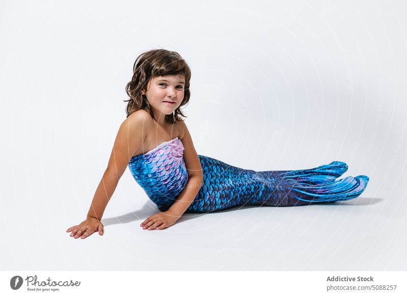 Charming girl sitting in studio in mermaid costume kid tail scale shimmer creative fantasy festive smile cheerful joy adorable little child childhood blue