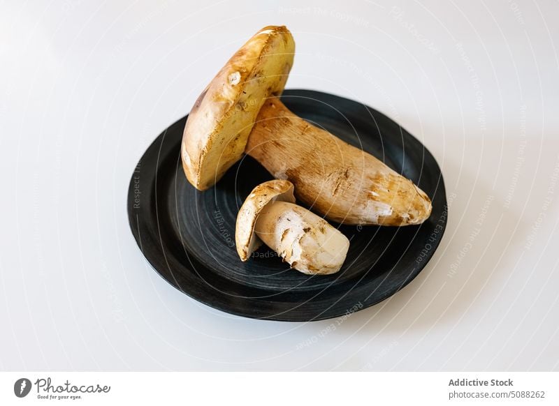 Raw mushrooms on black plate ceramic round minimal food raw ingredient uncooked edible porcini table fresh tableware simple gastronomy organic studio shot vegan