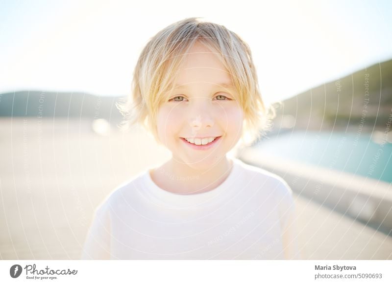 Portrait of cheerful smiling schoolboy child by sea during summer holidays on sunny day. Concept of freedom, happy childhood and limitless possibilities.