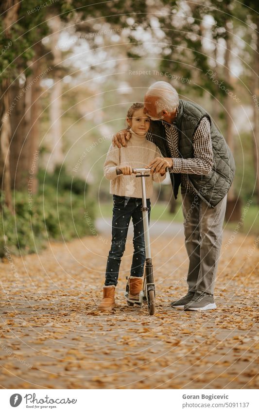 Senior man teaching his granddaughter how to ride kick scooter in park love caucasian elderly kid holiday vehicle spring happiness season grandfather alley