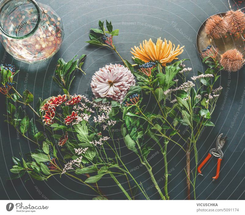 Beautiful chrysanthemum flowers and glass vase with bokeh on dark table. Top view. Flowers arrangements making. Florist workplace beautiful top view