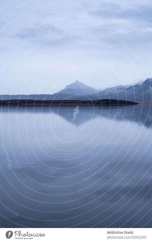 Frozen lake near snowy high mountains frozen quiet ice terrain overcast cloudy sky gray formation cold nature weather winter uneven gloomy environment climate