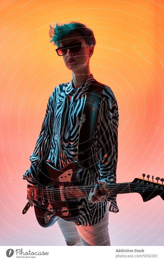 Stylish woman playing guitar in colorful studio electric music style musician guitarist trendy hipster fashion outfit sunglasses instrument melody sound female