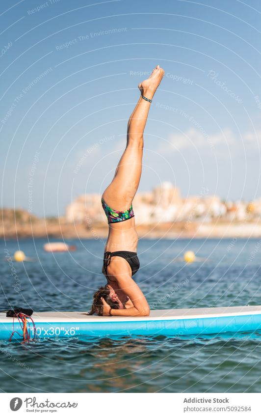 Slim woman in swimwear doing headstand on paddleboard sup board yoga sea water tranquil asana ripple aqua female slim practice balance pose position mindfulness