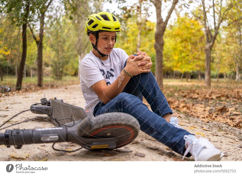 Teenage boy fell off electric scooter having pain teenage fall injury hurt knee problem young sit ground accident help suffer wound ache risk vehicle park