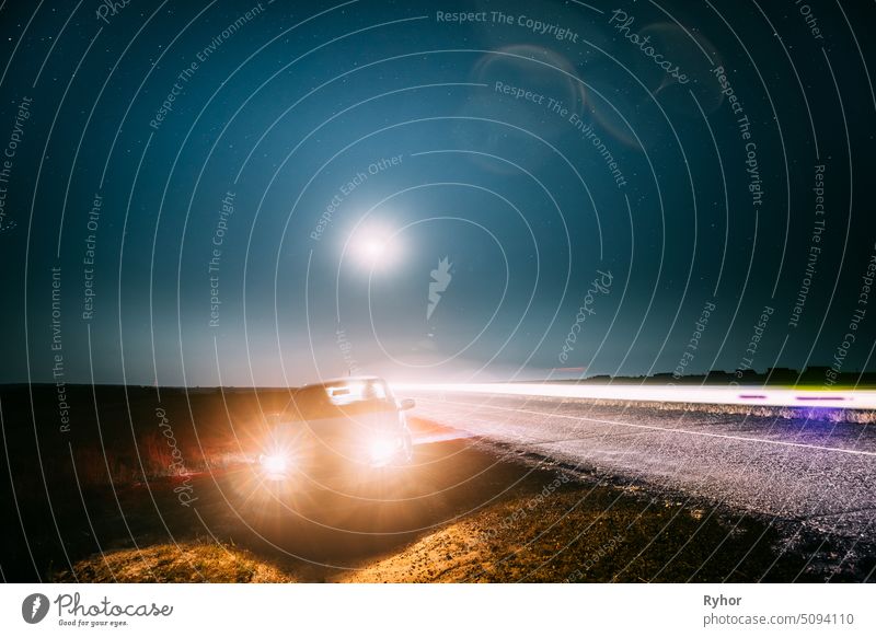 Night Starry Sky Above Country Asphalt Road In Countryside. Sedan Car Parking Near Asphalt Road In Summer Night. Yellow Car Lights And Night View Of Natural Glowing Stars