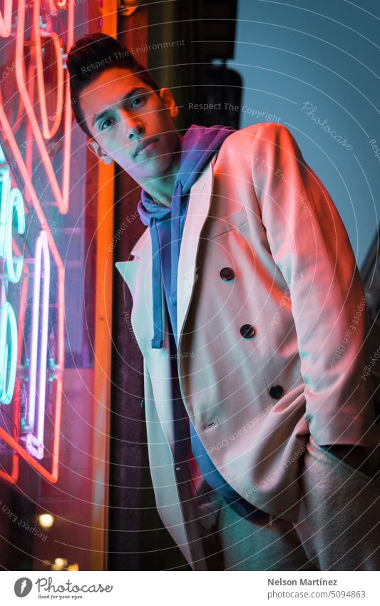 Portrait of young hispanic man with red neon light on the face, wearing a beige blazer street bright fashion suit party look leather night guy concept colourful