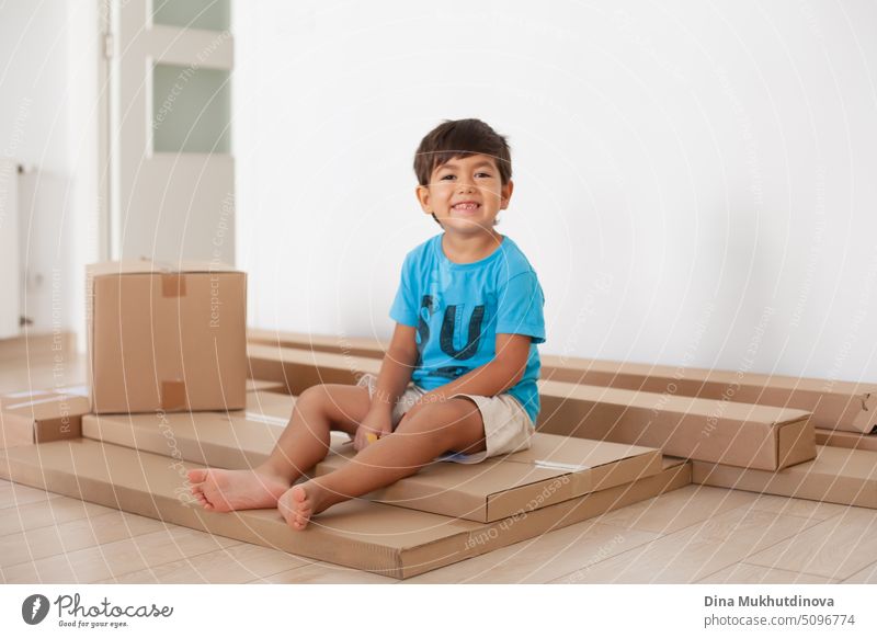 4 or 5 year old boy sitting on cardboard boxes, playing with packaging after moving to new home with his family. Joy of moving to a new apartment. Smiling kid holding a carton box.