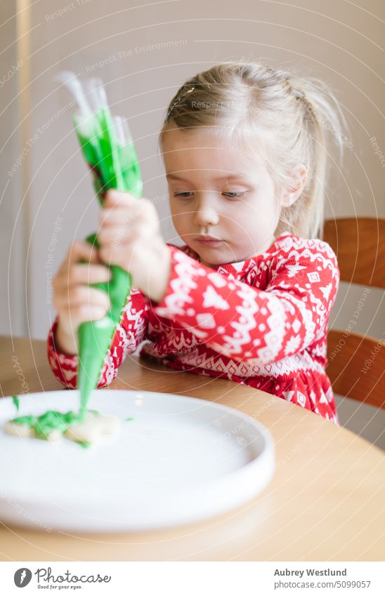 Little girl in red Christmas sweater decorating Christmas cookie icing food gingerbread homemade pastry sweet celebration festive table white baked sugar