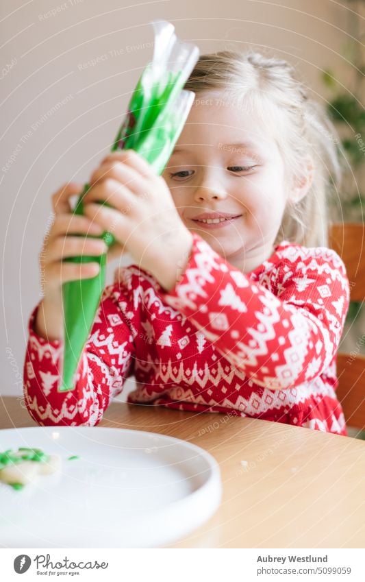 happy little girl decorating a Christmas cookie with green frosting christmas red holiday gift child winter white kid cute portrait sweater new year fashion