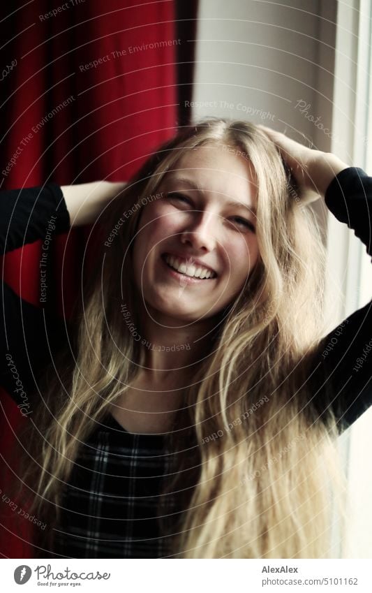 Close portrait of young blonde woman standing by the window smiling and holding her arms at the back of her head Woman Young woman Blonde Long-haired Smiling