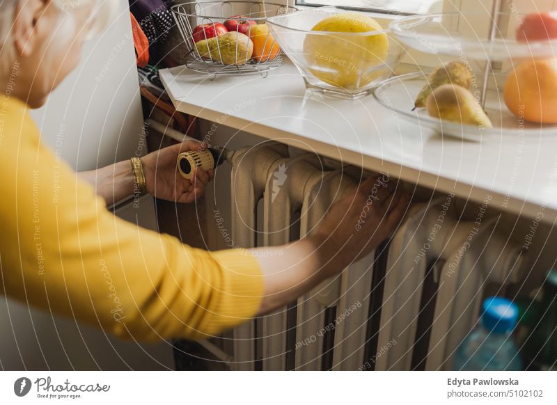 Woman adjusting the temperature of a radiator at home people woman senior mature female elderly house old domestic life pensioner retired real people adult