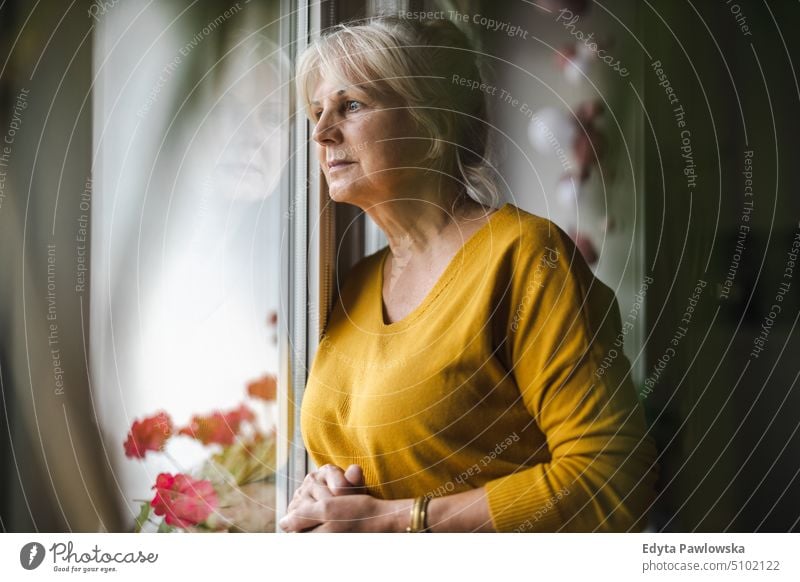 Worried elderly woman looking in window smiling happy enjoying positive people senior mature female home house old aging domestic life grandmother pensioner