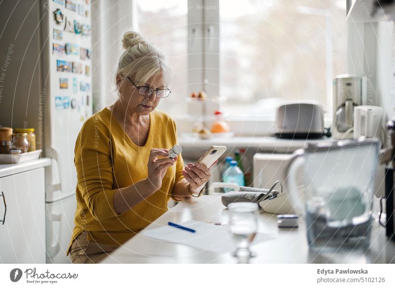 Older woman checking prescription with mobile phone people senior mature female elderly home house old aging domestic life grandmother pensioner retired