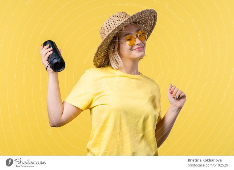 Lady dancing, enjoying on yellow studio background. She moves to rhythm of music. Young woman listening to music by wireless portable speaker - modern sound system.