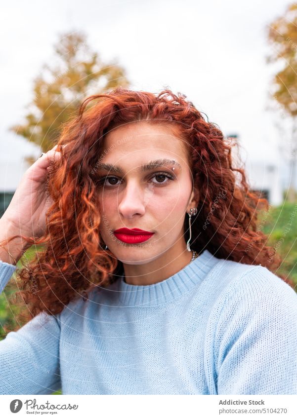 Young redhead lady standing on street and looking at camera woman confident style park millennial city female young long hair ginger hair delight red hair