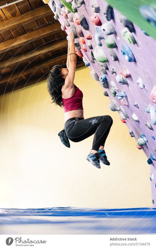 Female climber hanging on tilted wall sportswoman training gym grip practice female mat power bouldering extreme activity effort energy strong hobby athlete