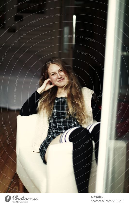 Portrait through balcony door of young blonde woman sitting diagonally in armchair portrait Woman Young woman Balcony French windows Armchair Legs Sock Dress