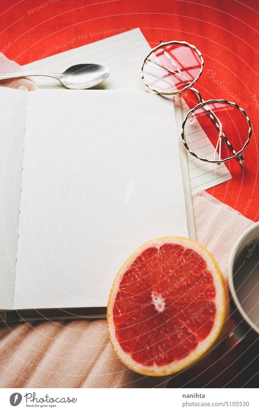 Colorful flat lay of an open diary surrounded by common objetcs as a work space mockup book page background blank white orange red grapefruit glasses notebook