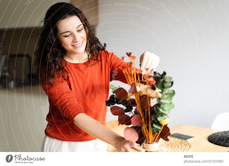 Young happy woman arranging dried flowers in a vase decorating home dry setting table eucalyptus bouquet kitchen young beautiful smiling orange green decoration