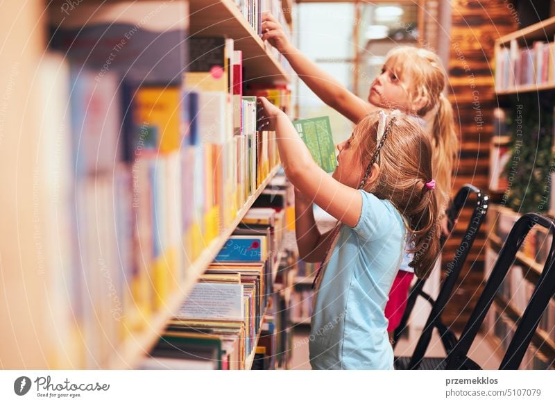 Schoolgirls looking for books in school library. Students choosing set books. Elementary education. Doing homework. Back to school back schoolgirl child reading