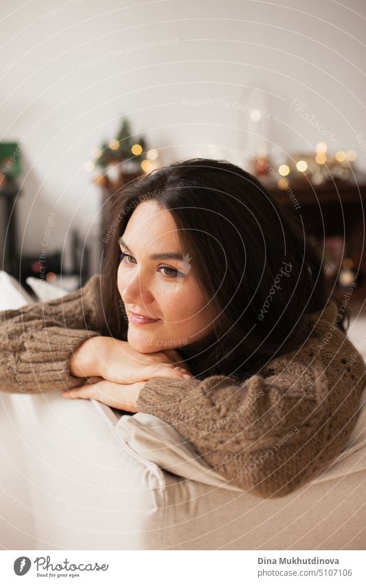 Beautiful caucasian woman smiling at her cozy home apartment leaning over the couch. Closeup casual lifestyle female portrait. Millennial living. Expat life. Creating comfortable space around you.