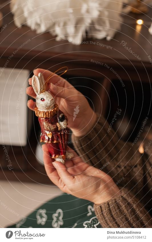 Woman holding vintage rabbit handmade ceramic artisanal in her hands. Christmas tree ornaments at home on the coffee table in traditional gold and red holidays color palette.