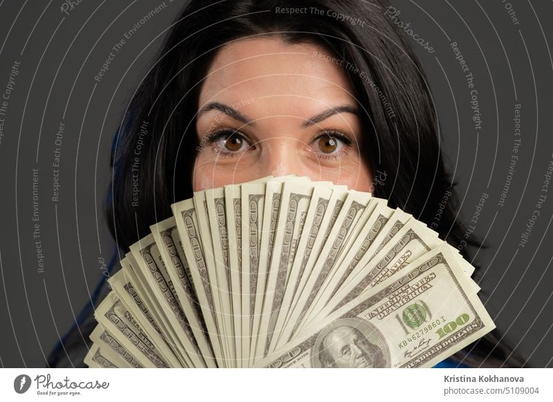 Satisfied happy excited adult woman showing money - U.S. currency dollars banknotes on grey wall. Symbol of success, gain, victory. portrait person business