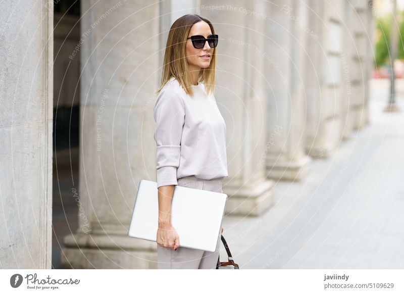 Businesswoman in sunglasses standing on street businesswoman laptop city confident commute urban style outfit gadget handbag freelance building positive