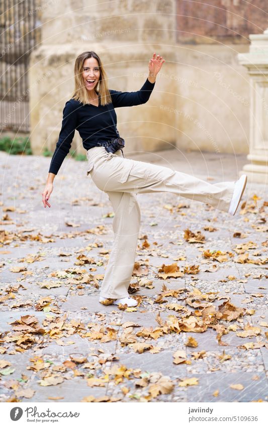 Cheerful young woman kicking fallen leaves while walking in park smile holiday autumn tourist cheerful vacation enjoy leaf positive delight female casual