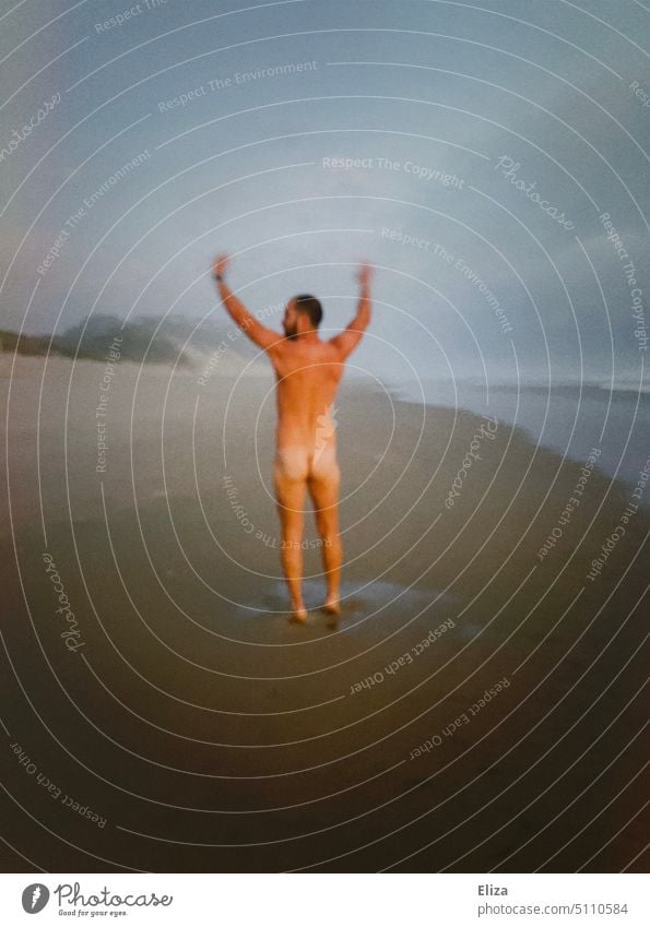 A man stands naked with white butt and arms raised on the beach Man Naked nudity Beach behind bottom White Bottom Back Adults Skin Naked flesh Masculine