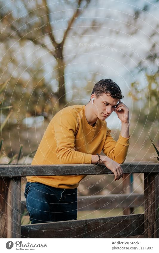 Pensive man standing on wooden bridge pensive earphones listen music footbridge autumn park lean male gadget fall young thoughtful casual device connection