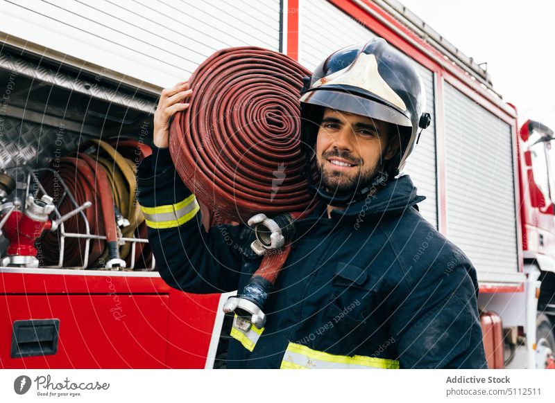 Hispanic fireman in helmet carrying hose on shoulder smile fire engine work uniform portrait male adult hispanic ethnic truck glad friendly job daytime happy