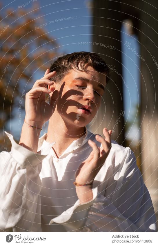 Transsexual man with makeup standing near columns in sunlight transsexual lgbtq extravagant non binary gender fluid park queer androgynous personality male