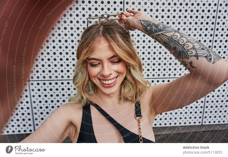 Delighted young trendy woman taking selfie and smiling on street self assured smile cheerful style positive happy self portrait adjust glad cool female blond