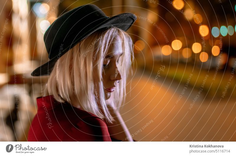 Portrait of young woman with blond hairstyle and hat on night glowing european city background. Nose piercing. person nightlife lifestyle female girl beautiful