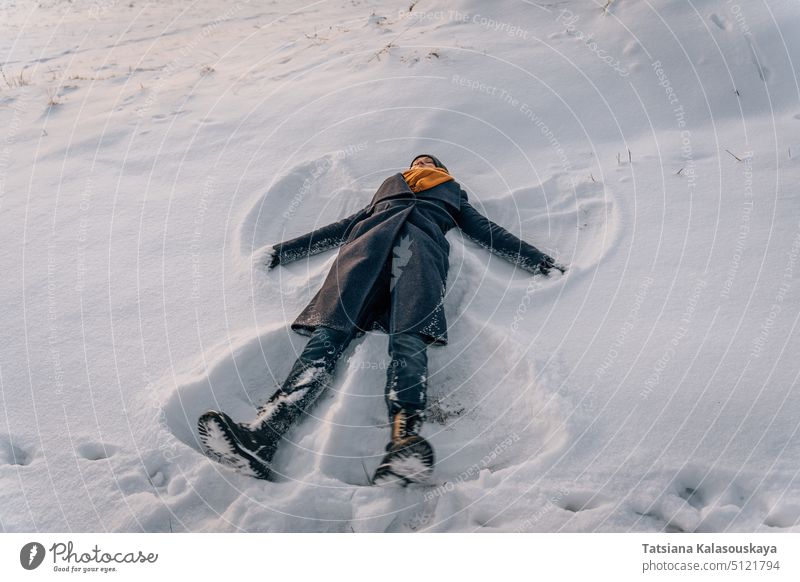 A woman lies in the snow in the shape of a snow angel in winter female people person European White adult mid adult one Single person orange cold Enjoy Liking