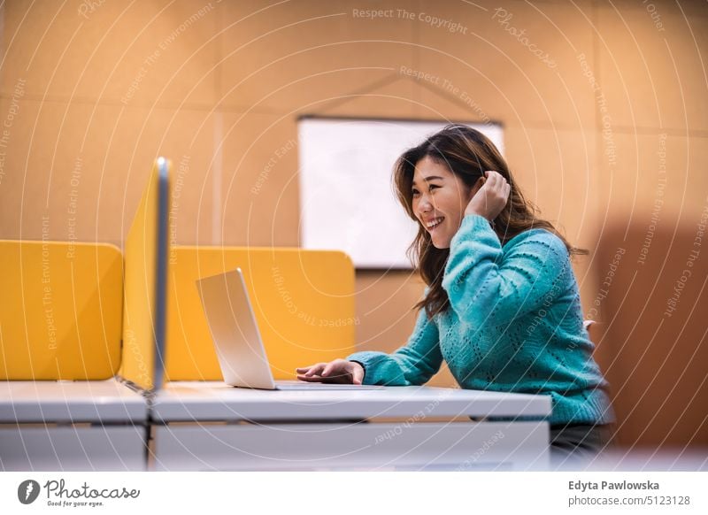 Female student working on laptop in a library cubicle computer online using laptop technology education learning university university student studying