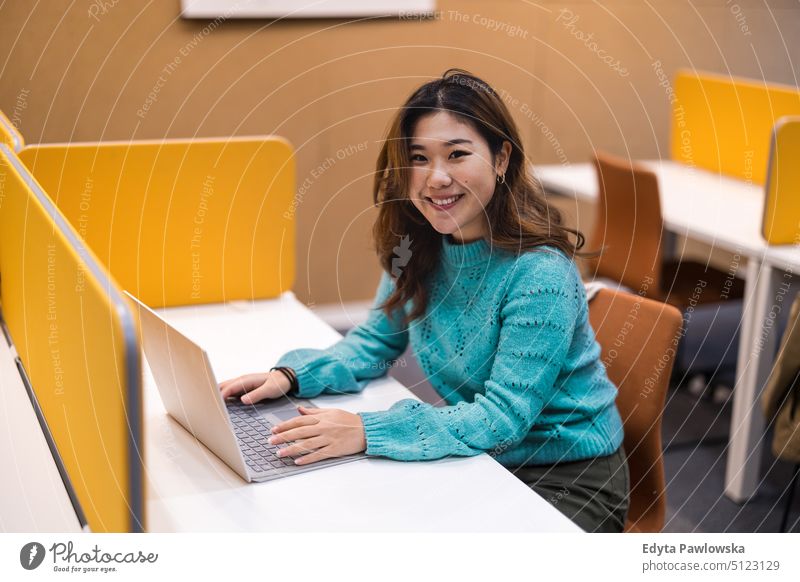 Female student working on laptop in a library cubicle computer online using laptop technology education learning university university student studying