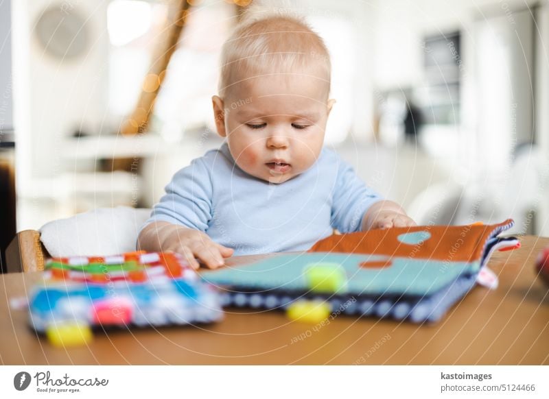 Happy infant sitting at dining table and playing with his toy in traditional scandinavian designer wooden high chair in modern bright atic home. Cute baby playing with toys