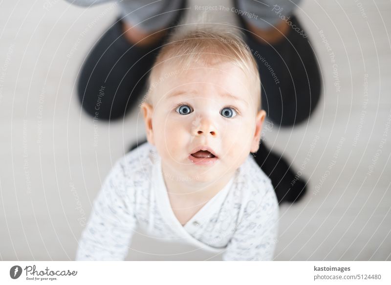 Top down view of cheerful baby boy infant taking first steps holding to father's sweatpants at home. Cute baby boy learning to walk little child happy dad small