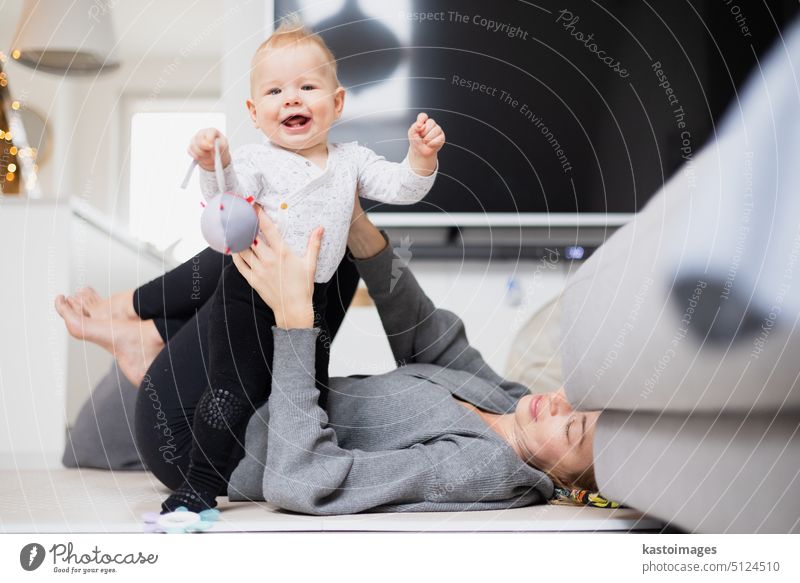 Happy family moments. Mother lying comfortably on children's mat playing with her baby boy watching and suppervising his first steps. Positive human emotions, feelings, joy.